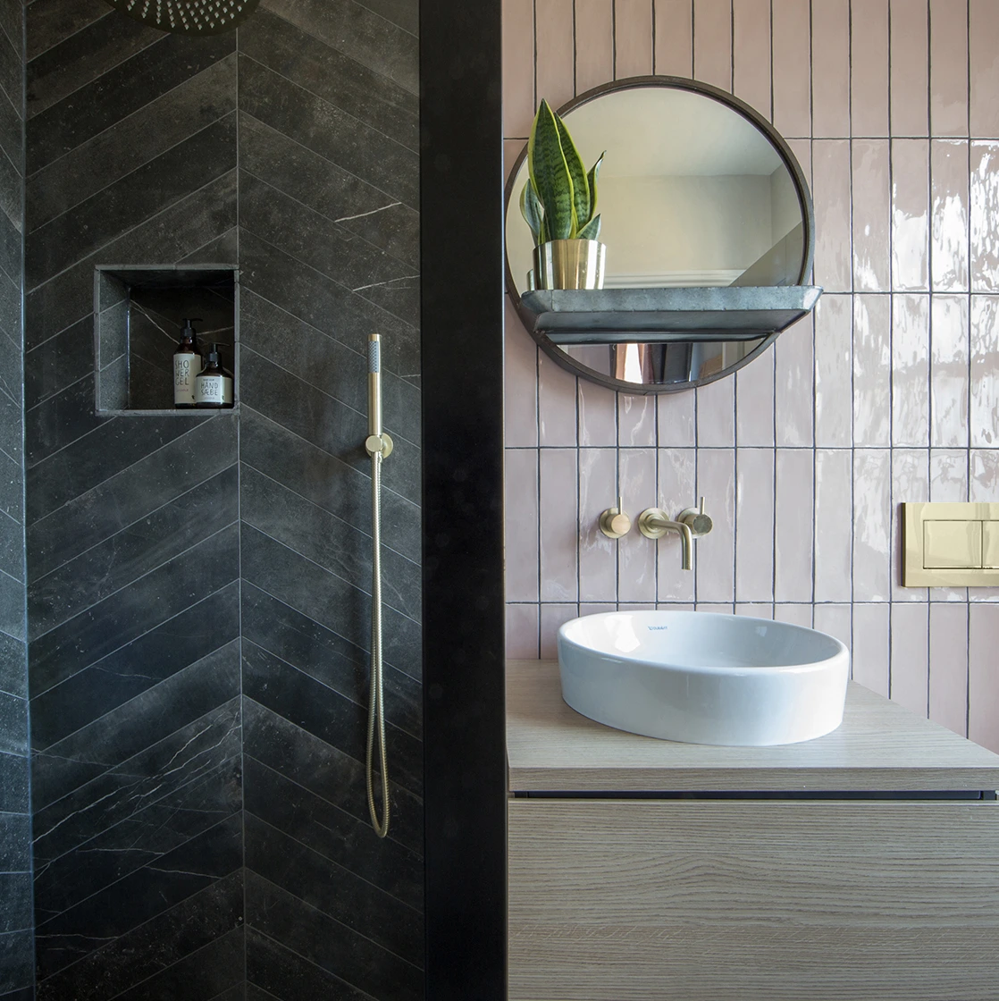 Bathroom with dark stone shower, pink tiles and a circular mirror