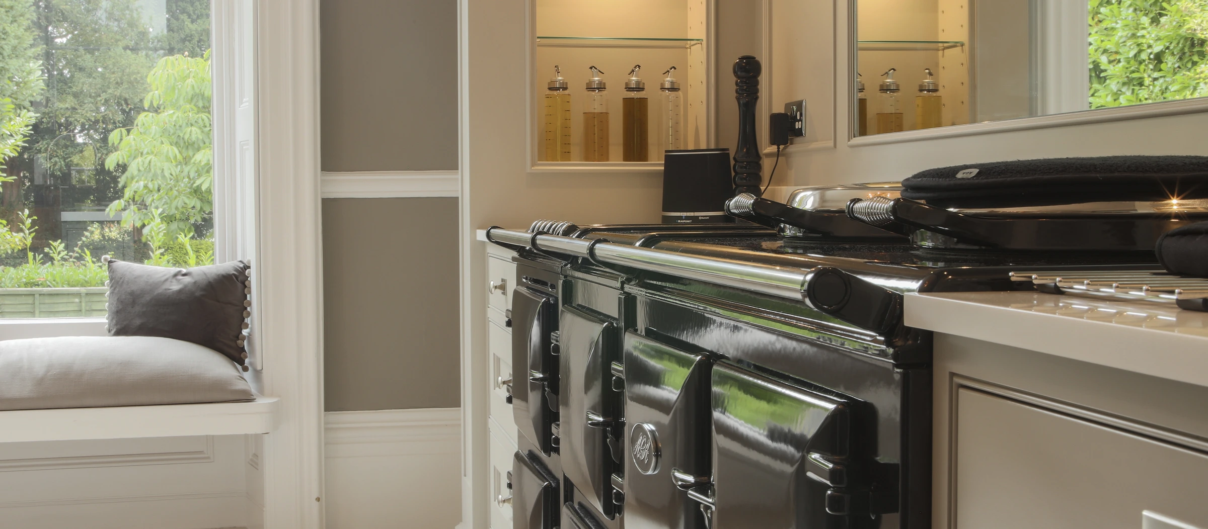 A traditional dark green range cooker beside a sunlit window seat in a bespoke kitchen